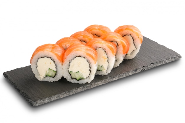 Sushi Rolls con salmone, cetriolo, foglia di nori e crema di formaggio all'interno su ardesia nera o pietra scisto superficie isolata