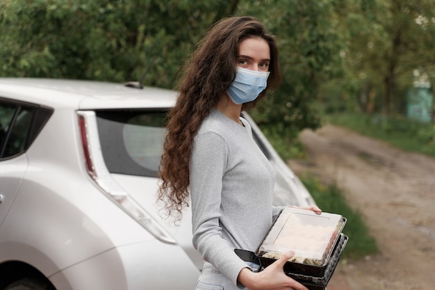 Sushi set in scatola servizio di consegna cibo sano in auto. Il corriere della ragazza in maschera medica con 2 scatole di sushi si trova di fronte all'auto.