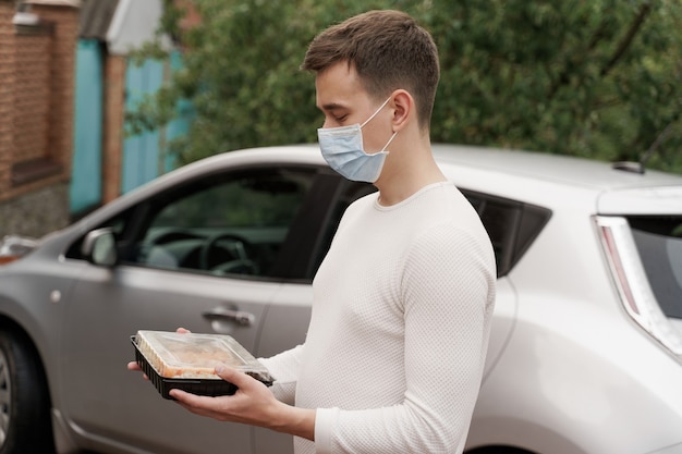 Sushi set in scatola servizio online di consegna cibo sano in auto. Un bell'uomo corriere in maschera medica ti dà una scatola di sushi. Cucina giapponese.