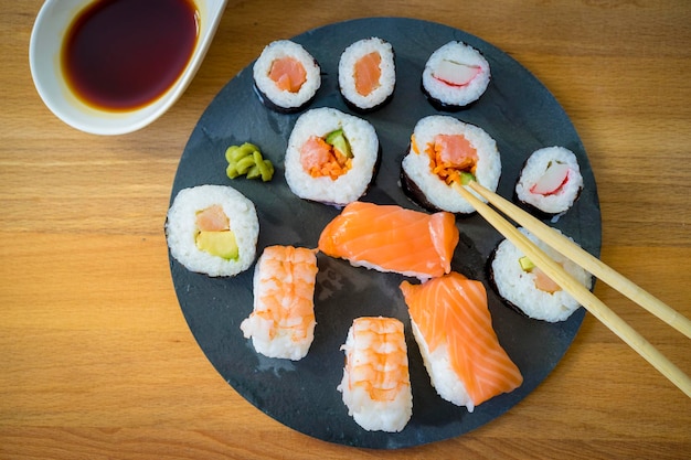 Sushi su un tavolo di legno sul piatto di ardesia nero con salsa di soia e bacchette