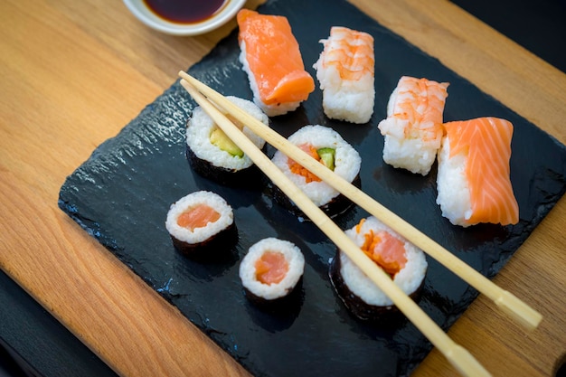 Sushi su un tavolo di legno sul piatto di ardesia nero con salsa di soia e bacchette