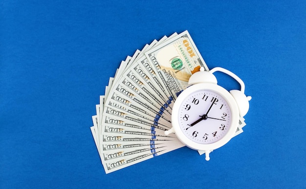 Sveglia bianca su banconote da un dollaro su sfondo blu Il tempo è denaro Il concetto di pianificazione aziendale e finanza