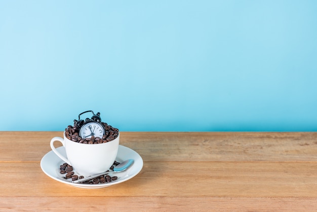 Sveglia e chicchi di caffè in tazza bianca sul tavolo di legno