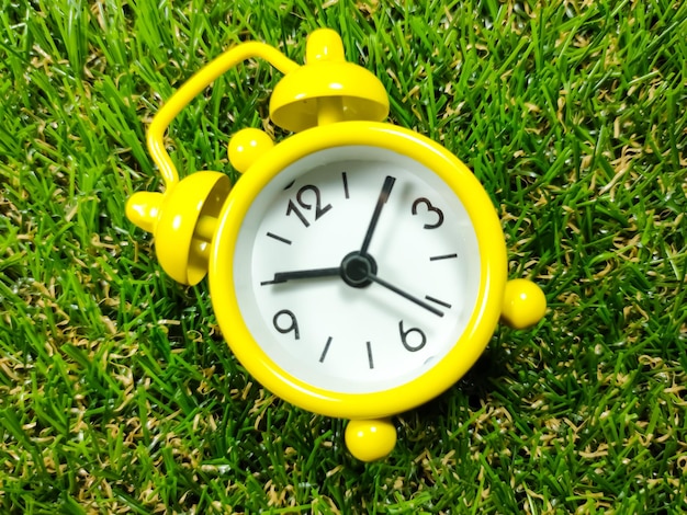 Sveglia sullo sfondo dell'erba Concetto di tempo Sveglia gialla con erba verde fresca con spazio di copia