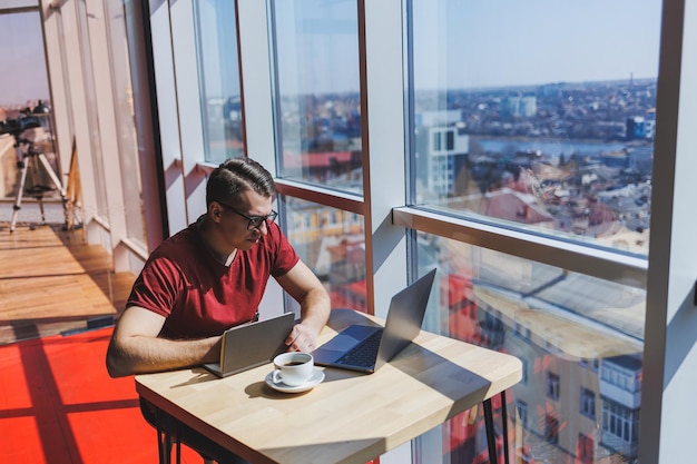 Sviluppatore di software intelligente seduto al desktop in uno spazio di coworking con laptop e creazione di idee editoriali utilizzando netbook per la messaggistica e il networking durante il lavoro freelance