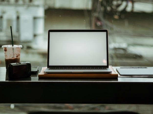 Svuoti il computer portatile dello schermo con la macchina fotografica ed il caffè di ghiaccio nel caffè.
