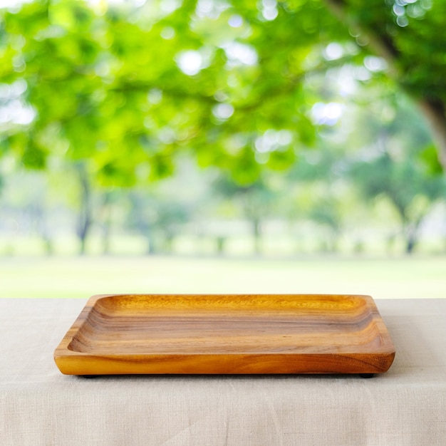 Svuoti il ​​vassoio di legno quadrato sopra il fondo del parco di verde della sfuocatura.