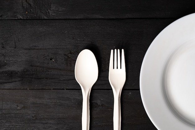 Svuoti la ciotola, la forchetta e il cucchiaio bianchi sulla tavola di legno nera, vista del primo piano. Concetto di dieta: disposizione piana di piatti puliti della cucina su una superficie rustica scura