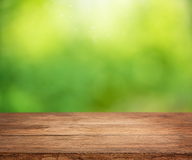 Svuoti la tavola di legno con il fondo verde astratto defocused soleggiato della natura.