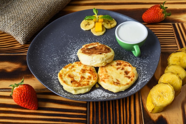 Syrniki o pancake al formaggio con salsa di panna e banane su un piatto sul tavolo di legno da vicino