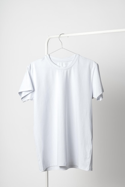 T-shirt bianca semplice appesa a un appendiabiti contro la parete bianca