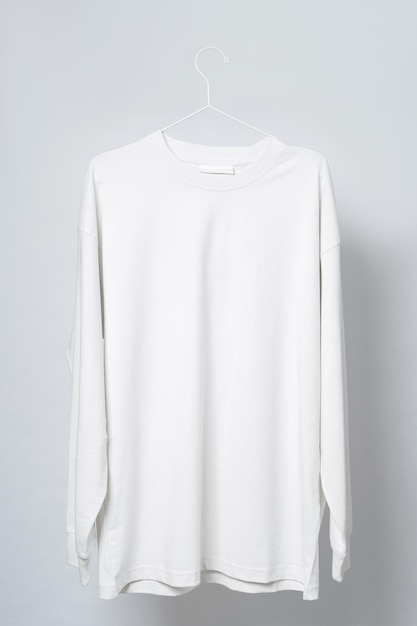 T-shirt bianca vuota a maniche lunghe appesa al sottile gancio metallico su sfondo grigio chiaro