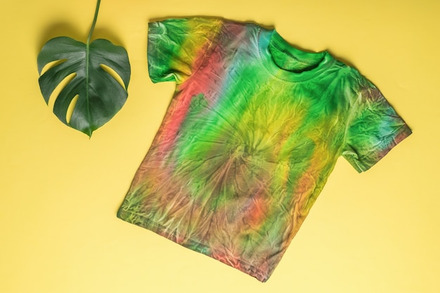 T-shirt in stile tie dye su fondo giallo con foglia verde. Colorare i vestiti a mano a casa. Disposizione piatta.