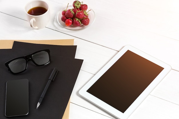 Tablet, foglio bianco, bicchieri e tazza di caffè sulla tavola di legno dell'ufficio. Sfondo bianco. Vista dall'alto. Copia spazio. bagliore di sole