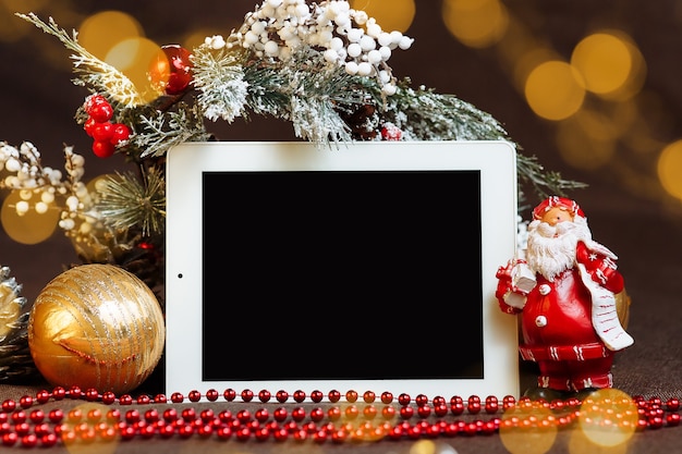 Tablet orizzontale con uno schermo vuoto tra i punti salienti delle decorazioni natalizie e il mock up di babbo natale