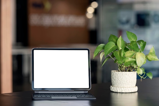 Tablet portatile con schermo bianco vuoto mockup con tastiera magica su tavolo di legno in una stanza ufficio tono scuro.