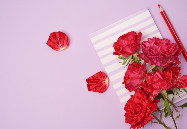 Taccuino chiuso e un mazzo delle rose rosse su una porpora