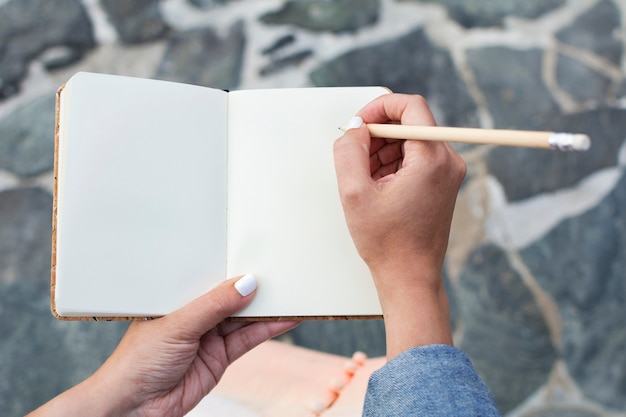 Taccuino del documento in bianco e le mani della donna con la matita di legno da scrivere.