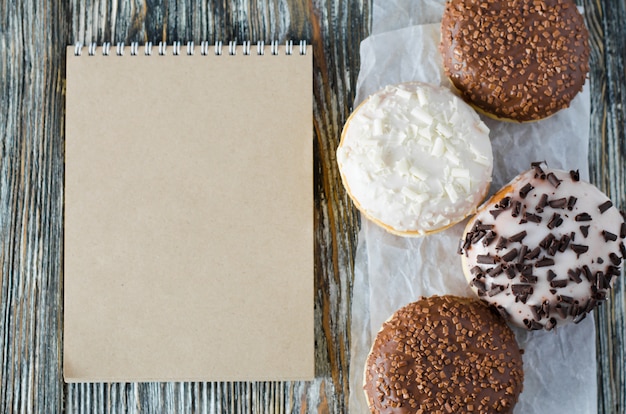 Taccuino e ciambelle assortite con cioccolato glassato su superficie di legno