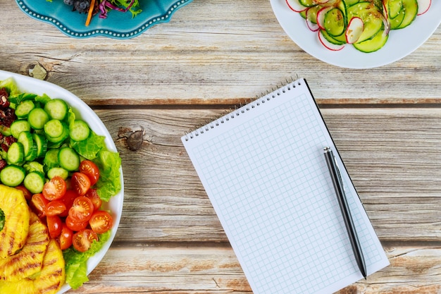 Taccuino e penna con insalate healty sulla tavola di legno