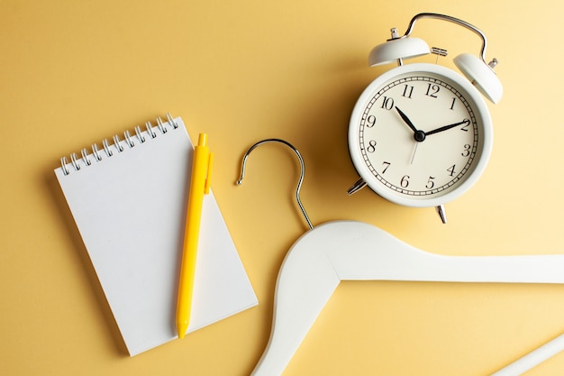 Taccuino in bianco per testo, una gruccia per vestiti e un orologio bianco su un fondo giallo