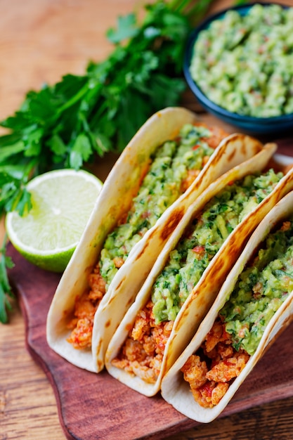 Tacos con carne macinata fritta e salsa guacamole su tavole di legno. Tacos messicani, coriandolo e lime su fondo di legno. Cucina messicana. Stile rustico