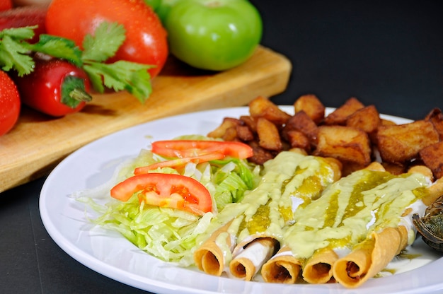 Tacos di pollo fritto conditi con panna e salsa verde accompagnati da insalata e patatine fritte