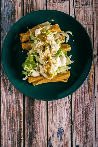 Tacos flauta con crema di formaggio e lattuga su un tavolo di legno Snack messicani