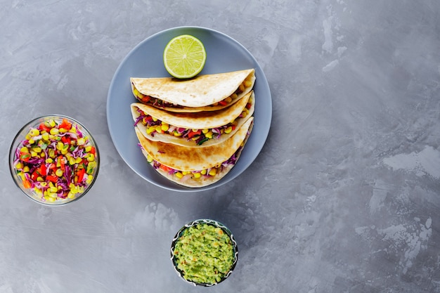 Tacos messicani con verdure e guacamole su sfondo grigio. Tacos vegani con mais, cavolo viola e pomodori su un piatto grigio. Copia spazio. Vista dall'alto