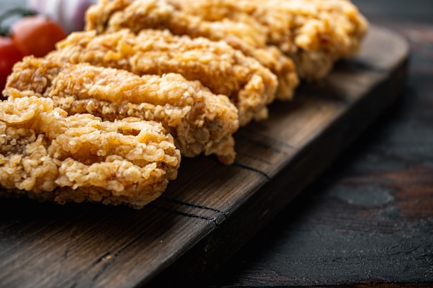 Tagli di ali di pollo impanate sulla vecchia tavola di legno scuro.