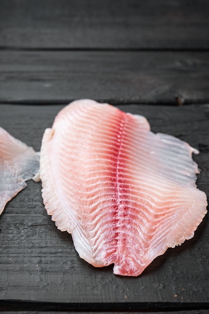 Tagli di carne di filetto di pesce tilapia cruda, sulla tavola di legno nera