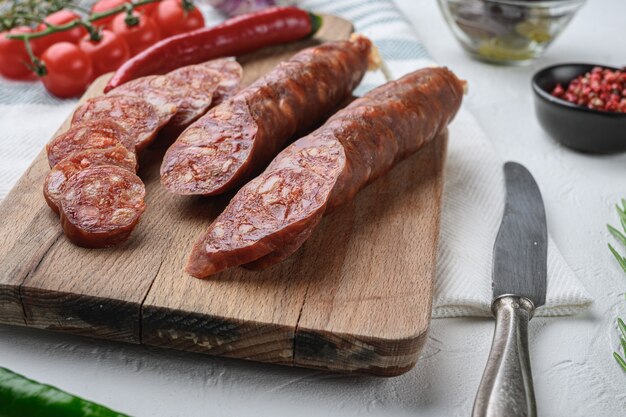 Tagli di chorizo tradizionali con spezie e ingredienti sulla superficie bianca.