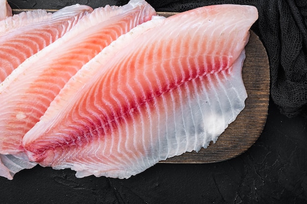 Tagli di filetto di pesce bianco crudo, sul tavolo nero, vista dall'alto