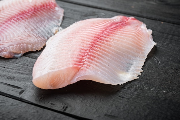 Tagli di filetto di pesce tilapia bianco sulla tavola di legno nera