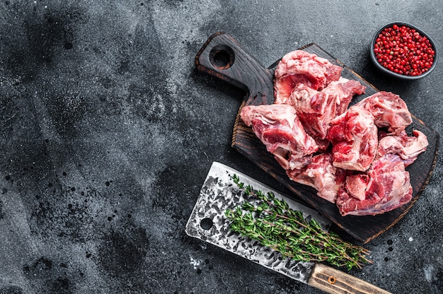 Tagli di stufato di carne di agnello crudo con osso su tavola di legno del macellaio e mannaia. Nero