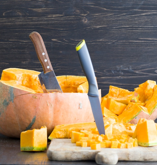 Taglia a pezzi una zucca arancione matura in ottobre, primo piano del cibo e dell'inventario per le vacanze di Halloween, accanto a coltelli affilati