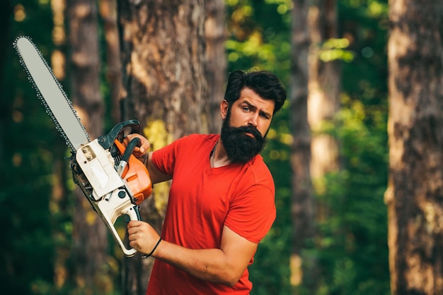 Taglialegna professionista che tiene la motosega nella foresta porta un bel giovane con la barba