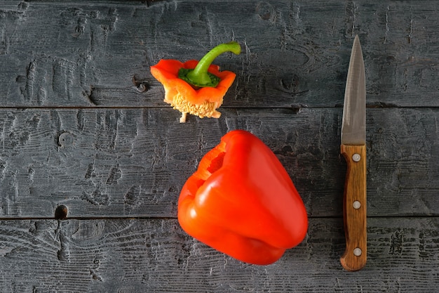 Tagliare con un coltello peperone rosso maturo su una tavola nera. Cibo vegetariano. La vista dall'alto. Lay piatto.