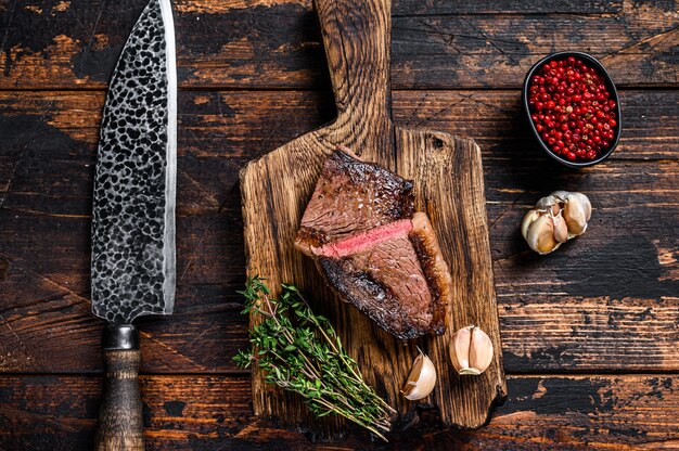 Tagliare il berretto fritto o la bistecca di carne di manzo picanha brasiliana su una tavola di legno. Fondo in legno scuro. Vista dall'alto.