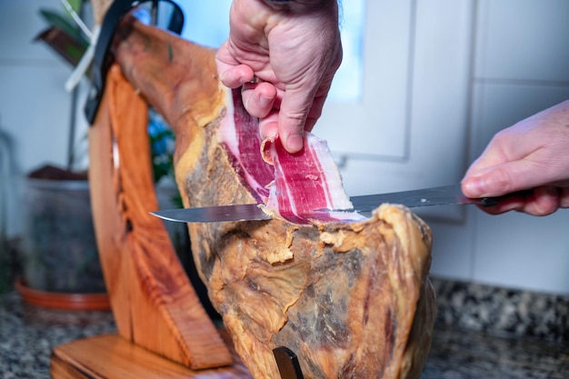 Tagliare il prosciutto iberico su un porta prosciutto in una cucina