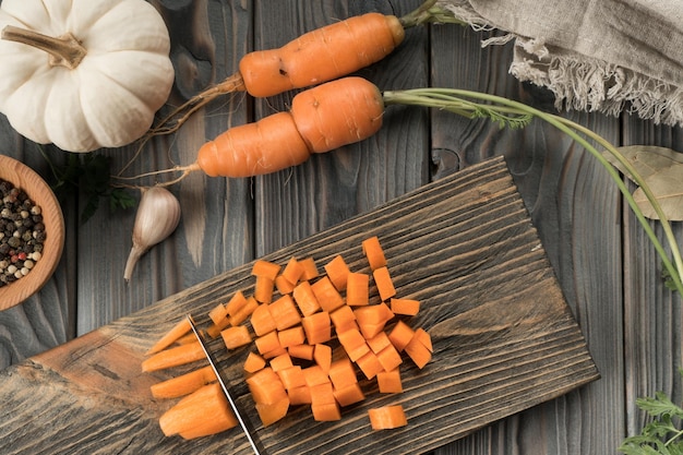 Tagliare la carota arancione cruda matura a cubetti sulla tavola di legno della cucina Carota tagliata a dadini con coltello Vista piatta Cibo sano