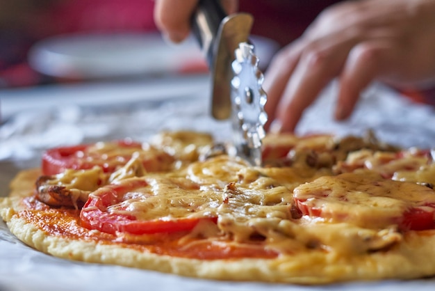 Tagliare la pizza fatta in casa a mano femminile affettare la pizza appena sfornata vista del primo piano di una mano del fornaio