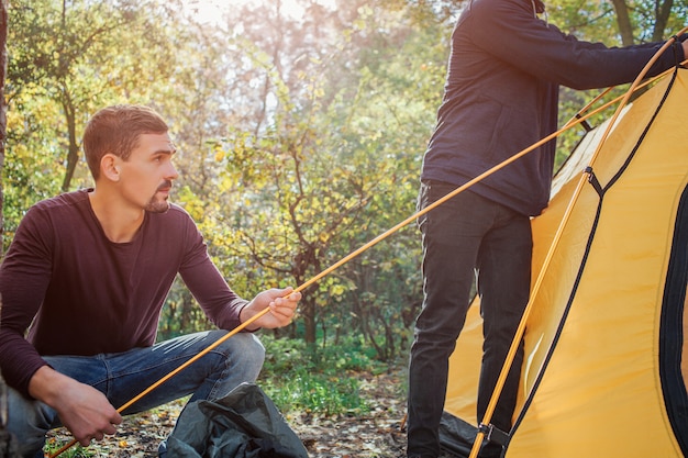 Tagliare la vista di due uomini che lavorano. Prima tiene la corda mentre un altro tocca la tenda. Sono nella foresta.