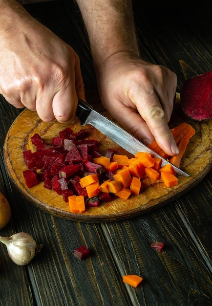 Tagliare le carote e le barbabietole bollite in piccoli pezzi per preparare la vinaigrette Coltello nella mano dello chef Concetto di piatto di verdure o cucina nazionale ucraina