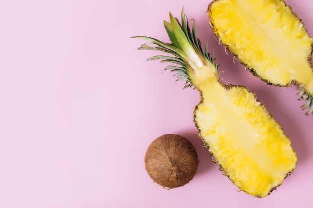 Tagliare le metà della frutta fresca di ananas con tutta la noce di cocco su sfondo rosa pastello