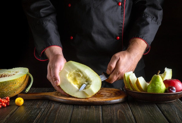 Tagliare un melone con un coltello nella mano dello chef in piccoli pezzi per servire un piatto di frutta Concetto di dieta a frutta Ambiente di lavoro sul tavolo della cucina