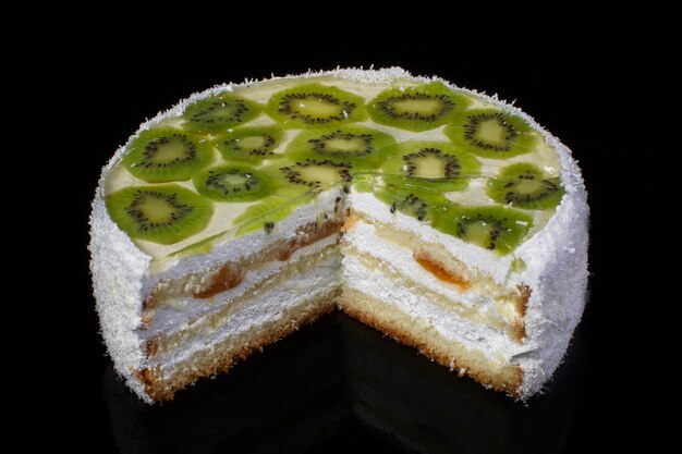 Tagliare un pezzo di torta bianca festiva con kiwi e scaglie di cocco su sfondo nero