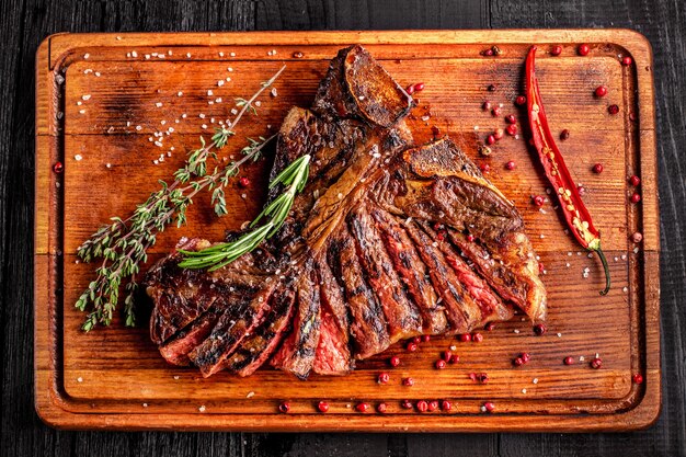 Tagliata di bistecca mediamente cotta alla griglia su tagliere rustico con rosmarino e spezie legno rustico scuro...