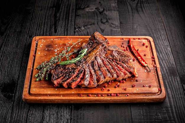 Tagliata di bistecca mediamente cotta alla griglia su tagliere rustico con rosmarino e spezie legno rustico scuro...