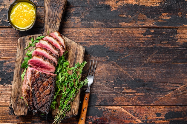 Tagliata di filetto di petto di anatra alla griglia. Fondo in legno scuro. Vista dall'alto. Copia spazio.